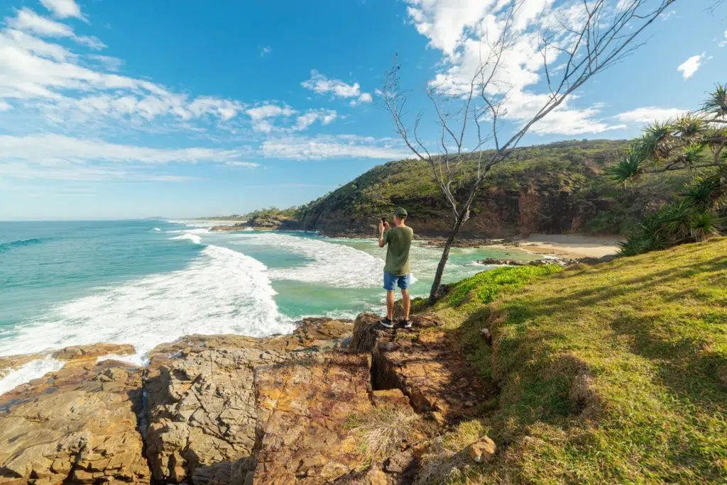 Young man standing on cliff edge and taking picture
